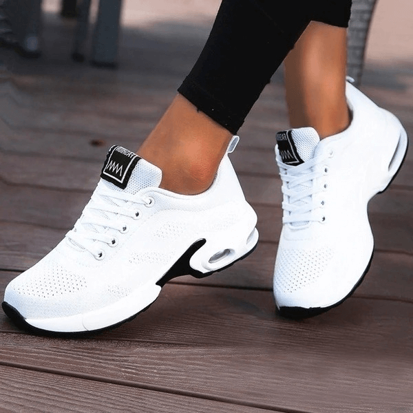 White breathable women's running shoes with lace-up closure, showing flexible movement on a wooden deck. Perfect for sports enthusiasts.